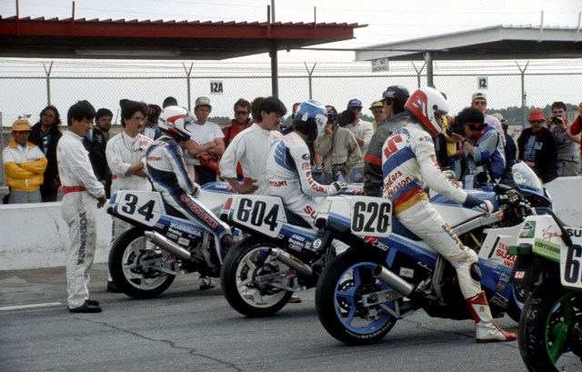 A group of Suzuki riders sits on pit road getting ready for the start of the 1987 Daytona 200. The Suzuki riders include Kevin Schwantz (34), Satoshi Tsujimoto (604) and Anders Andersson (626). (Larry Lawrence photo)