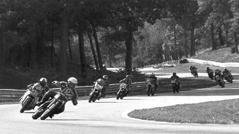 Lance David heads the pack just before the old Billy Mitchell Bridge at Road America. He’s leading Steve Tayler (49), Dean Joas (320), Ed Key (34) and the rest of the field in amid-1980s WERA C Superbike race. (Larry Lawrence photo)