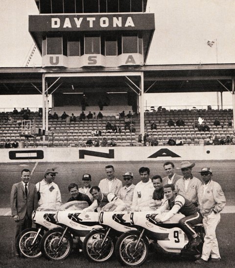 The Yamaha factory AMA Lightweight (250 Grand Prix) squad line up for a photo in front of the main grandstands at Daytona International Speedway in March of 1967. The riders in the photo (from left to right) are Tony Murphy, Robert Winters, Mike Duff and Gary Nixon. 