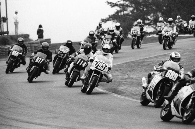 You can’t make out the first rider past the frame, but behind him are Jeff Taylor (No. 689), Charles Rosaly (793), Tripp Nobles (No. 114), W.C. Earnhardt (No. 617), Kelly Drew (No. 21), Anthony Arden (No. 189), Steve Craft (No. 131), Eric Turner (No. 543) and Joseph Ballard (No. 415) in the WERA A Superbike Novice Final at the 1989 GNF. Nobles broke through the field to win the race. (Larry Lawrence photo)
