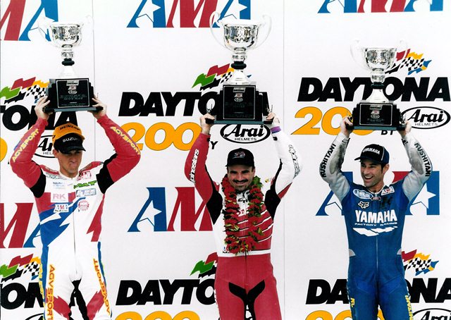 Duhamel '99 Daytona 200 podium The winners’ rostrum for the epic 1999 Daytona 200, one of the greatest AMA Superbike races in the history of the series. Honda’s Miguel Duhamel (center), in his comeback race after nearly losing his leg at Loudon the year before, nipped Suzuki star Mat Mladin in the second closest finish of the prestigious race. Longtime 250 Grand Prix ace Rich Oliver proved he was great on a Superbike as well. He edged Ben Bostrom at the line for third. (DIS photo)