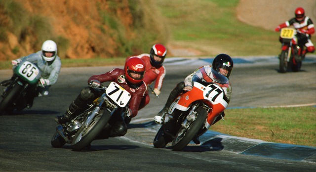 Conroy, Pat - GNF 1990 Vintage racing action at the 1990 WERA GNF with Pat Conroy (No. 77) with the inside line on his Harley-Davidson XR750 with Dave Roper (No. 71v) on a 500cc BSA challenging Conroy on the outside. Coming up behind Conroy and Roper are Ted Hubbard, on another BSA and Ron Barton (No. 85) on a Ducati 750. (Larry Lawrence photos)