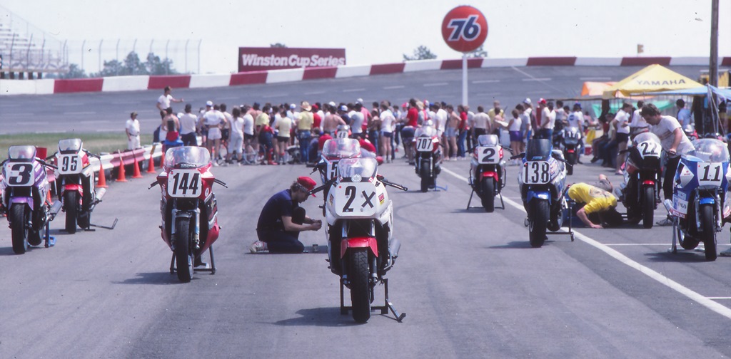 Some teams have already gridded their bikes before the start of a WERA National Endurance race at Rockingham in April of 1986. It looks like longtime WERA race director Ed Bargy is conducting the meeting. This shot from the end of the pits gives you a good illustration of the height of the banking the riders had to negotiate. (Larry Lawrence photo)