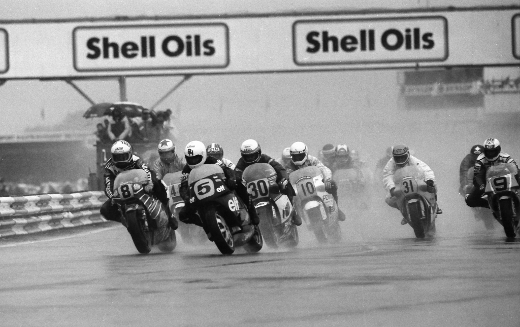 Ron Haslam (No. 5) rolls into a corner on the Elf 3 Honda NS500-powered GP machine at the rainy 1986 British 500cc Grand Prix at Silverstone. Haslam leads a pack of riders that includes Didier de Radigues (No. 8), Pier-Francesco Chili (No. 46), Roger Burnett (No. 30), Boet van Dulmen (No. 10), Simon Buckmaster (No. 31), Rob McElnea (No. 9) and others. (Photo by Henny Ray Abrams)